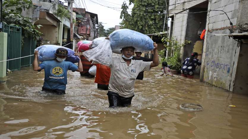 Indonesian men carry their belongings as they wade through the water at a flooded neighborhood following heavy rains in Jakarta, Indonesia.